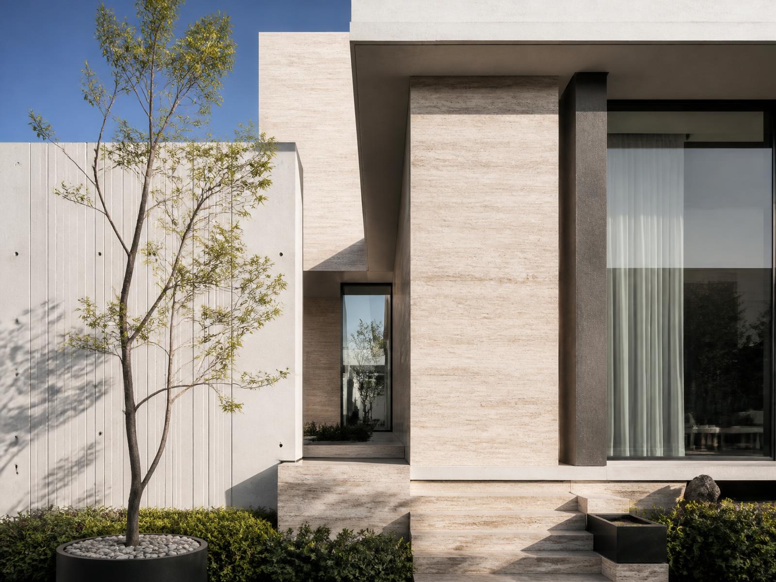 Contemporary residential architecture in travertine and concrete, photographed in strong daylight.